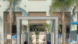 A building entrance with a gate, palm trees, and a tiled wall. - TUAREG Hotel (Maruggio)