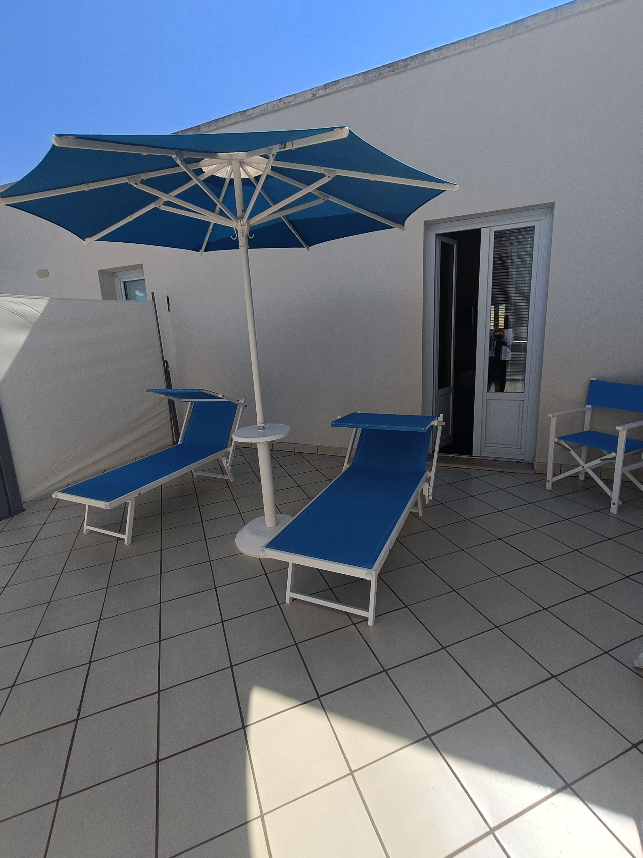 A sunlit outdoor seating area with blue lounge chairs and a large umbrella.