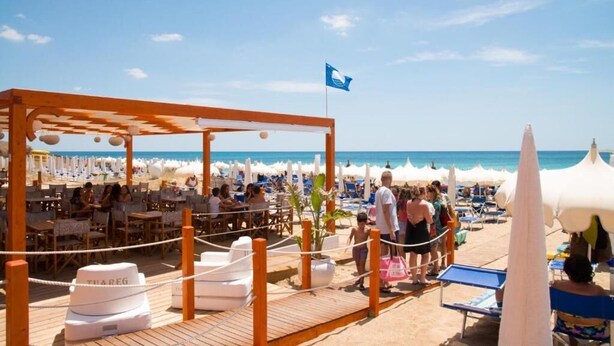 A beachside restaurant with outdoor seating, umbrellas, and a wooden deck. - TUAREG Hotel (Maruggio)