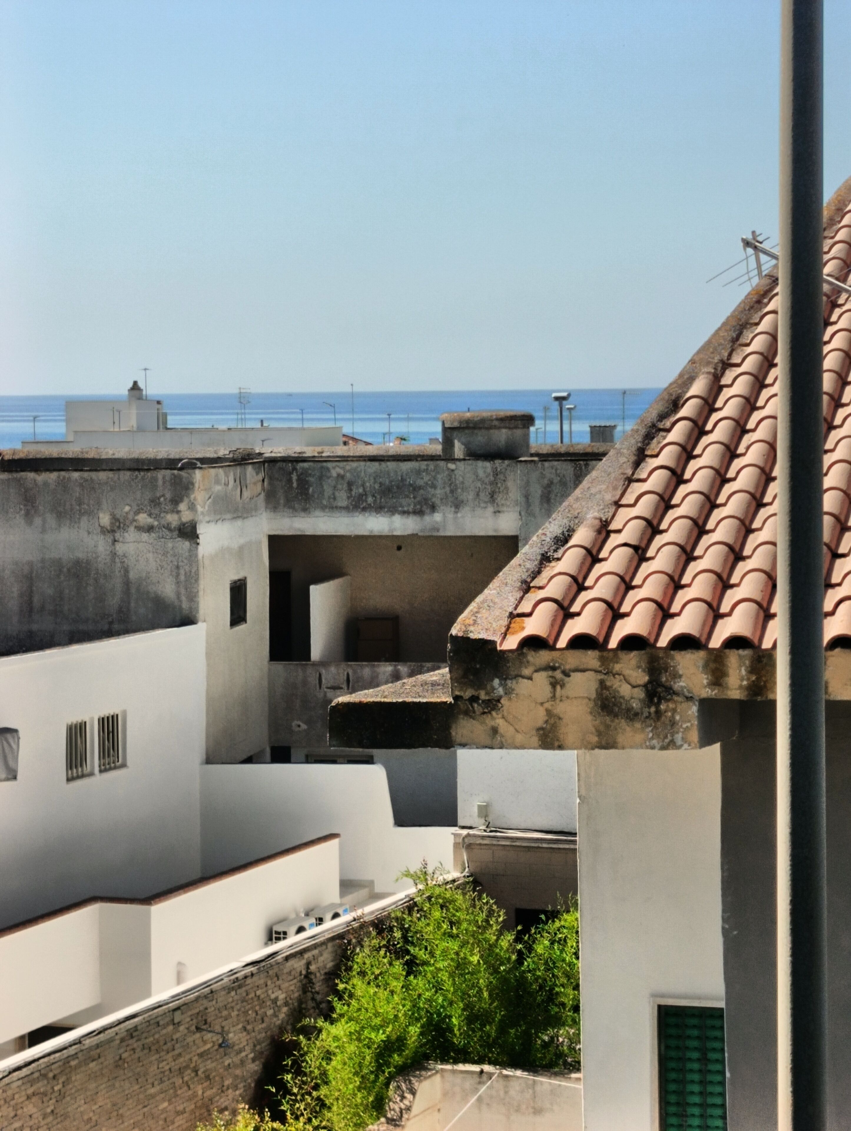 A rooftop view of buildings with a clear sky and a distant view of the sea.