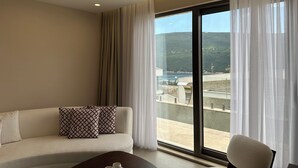 Una habitación de hotel moderna con un sofá, una silla y un ventanal con cortinas traslúcidas.