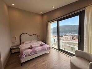 Een slaapkamer met een groot raam, een bed, een nachtkastje en een stoel.