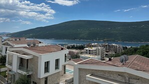 Zona residencial costera con edificios modernos, antenas parabólicas y vistas al mar y a una colina.