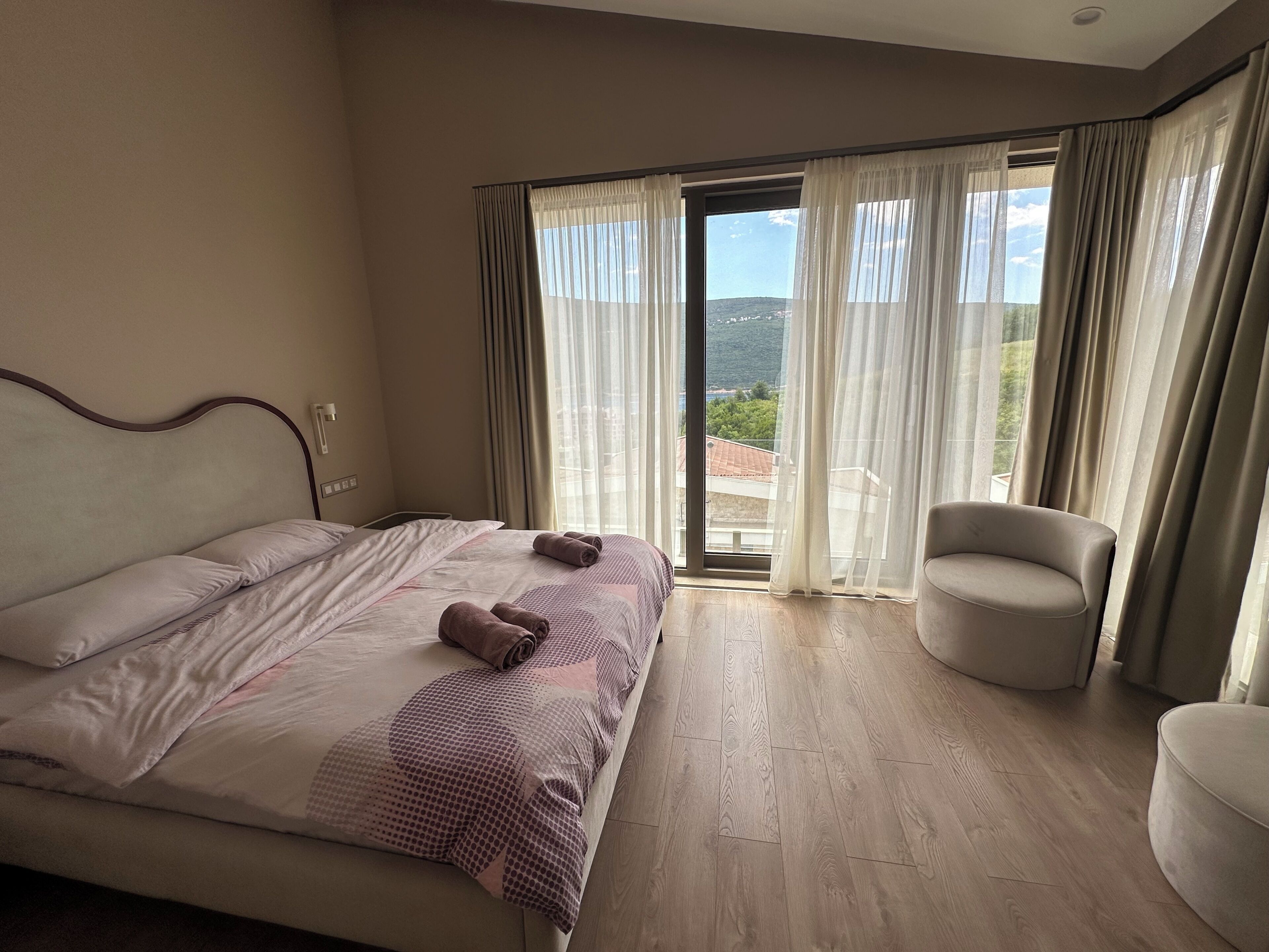 A bedroom with a bed, a chair, and a view of the outdoors.