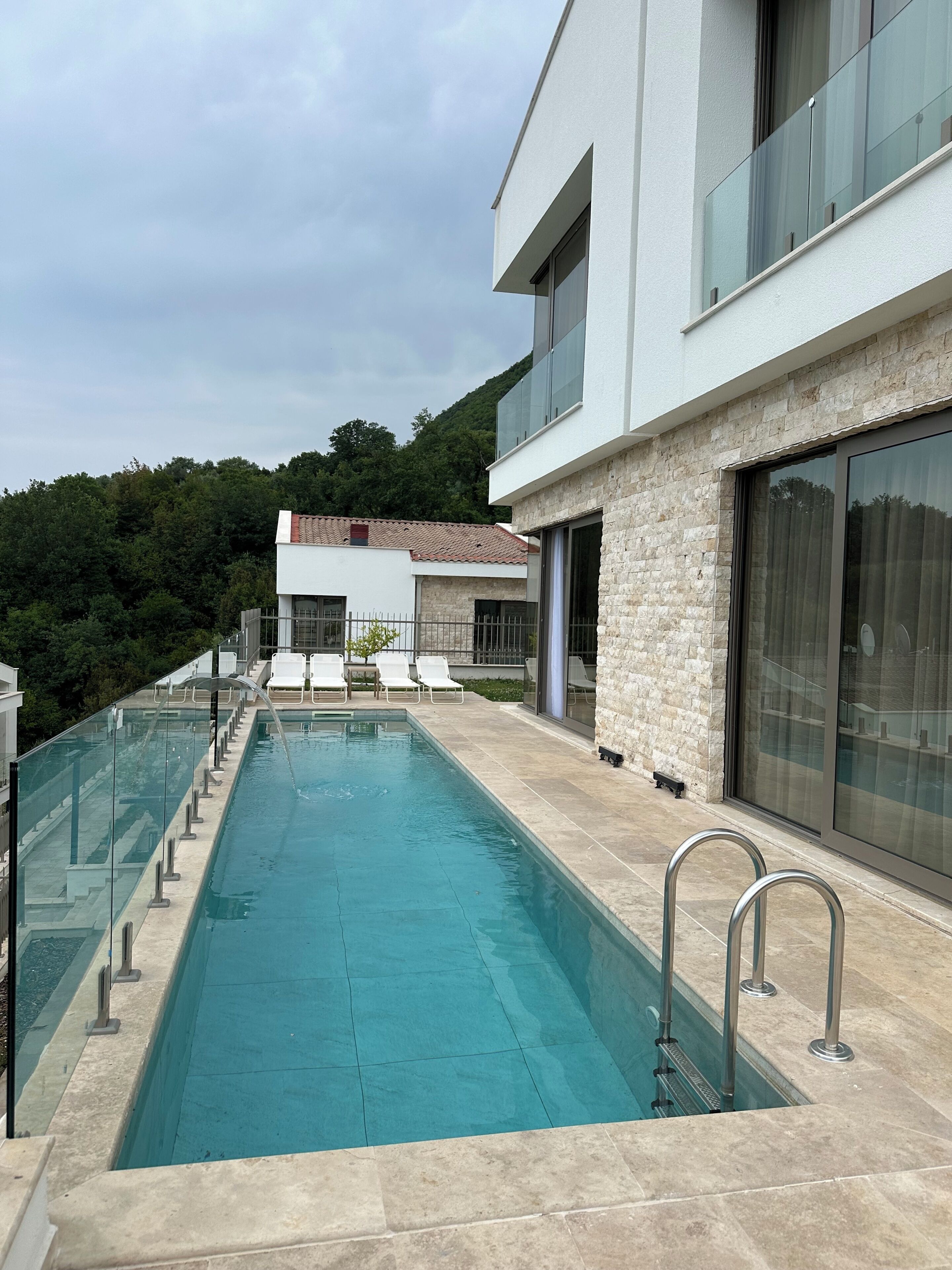A modern building with a swimming pool, stone facade, and glass railings.