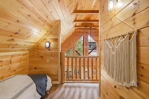 Ein Schlafzimmer einer Holzhütte mit Bett, Fenster, Deckenventilator und Blick ins Freie.