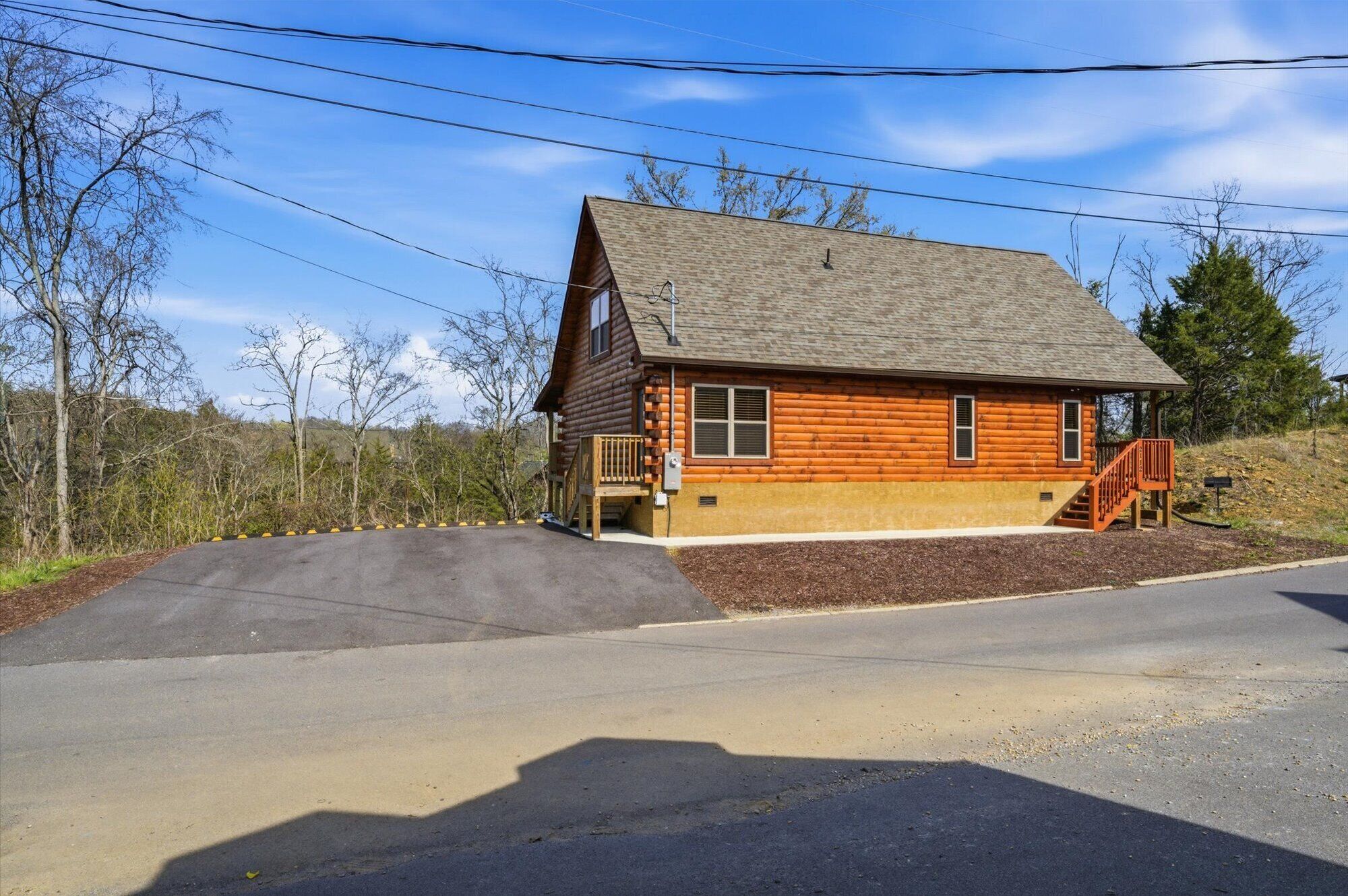 A log cabin with a porch, a driveway, and a clear sky.
