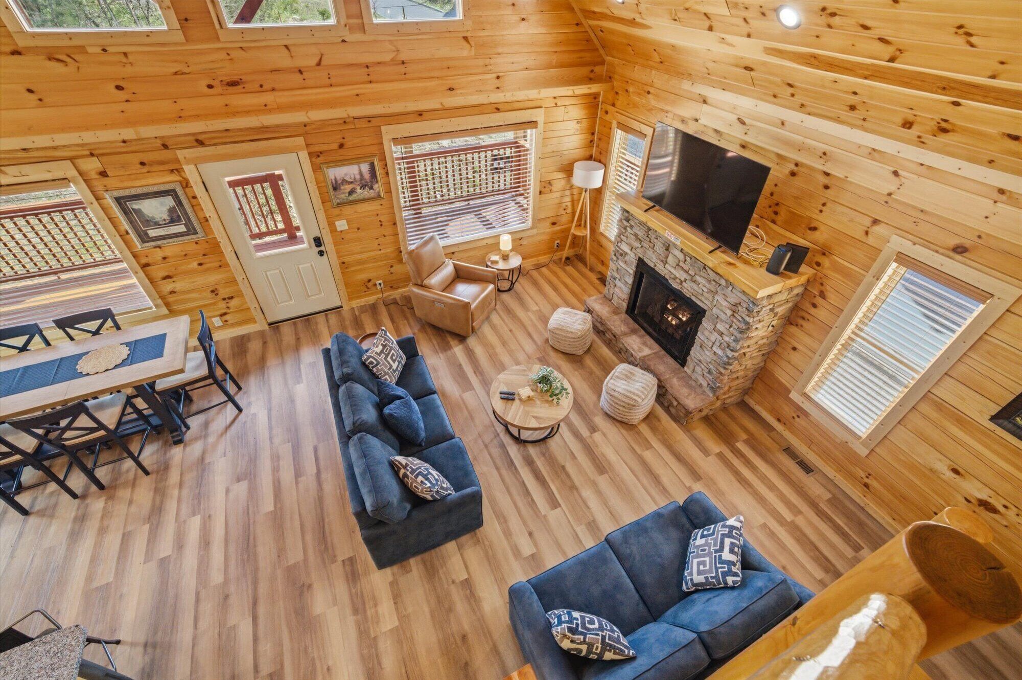 L’intérieur d’une cabane comprend une cheminée en pierre, des murs en bois, un canapé, une table à manger et un téléviseur.