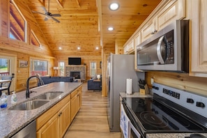 A cabin-style kitchen with wooden walls, granite countertops, stainless steel appliances, and a stone fireplace. - Morning Glory (Sevierville)