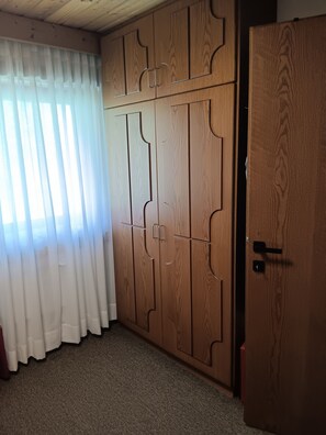 Ein Zimmer mit großem Holzschrank, Teppichboden und transparenten Vorhängen.