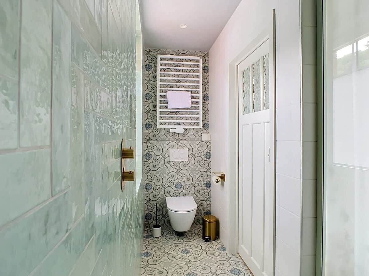 Een badkamer met patroon betegelde vloer, toilet, prullenbak en handdoekhouder.