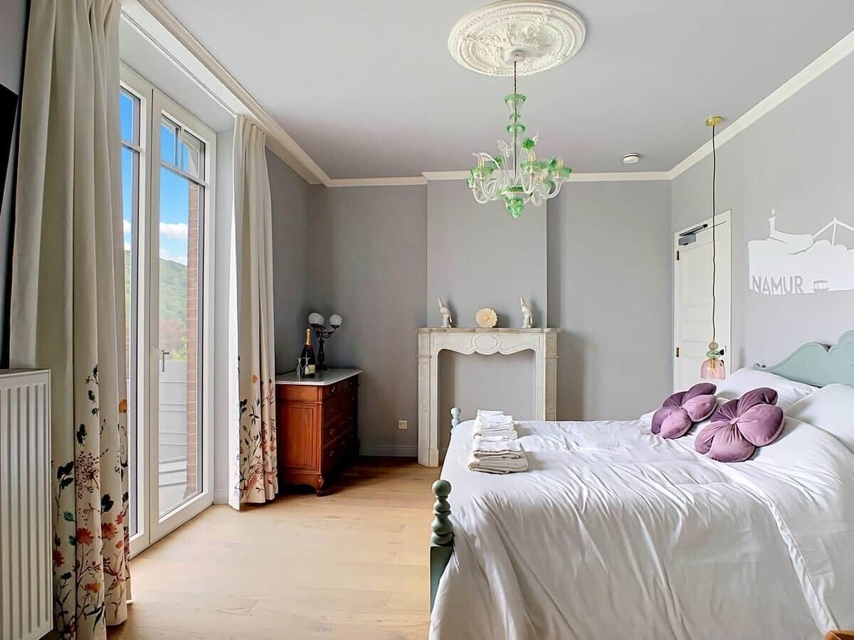 A bedroom with a bed, a dresser, a fireplace, and a view through a large window.