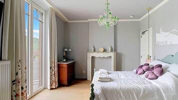 A bedroom with a bed, a dresser, a fireplace, and a view through a large window.