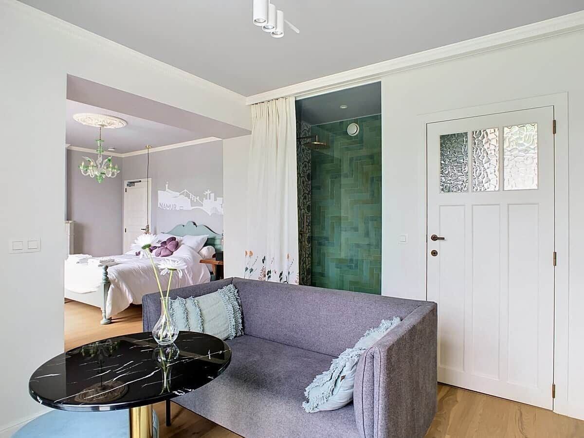 Una sala de estar moderna con un sofá gris, una mesa redonda negra con un florero, y una puerta con paneles de vidrio decorativos.