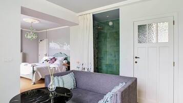 Una sala de estar moderna con un sofá gris, una mesa redonda negra con un florero, y una puerta con paneles de vidrio decorativos.