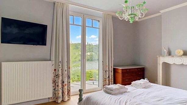 Ein Schlafzimmer mit Bett, Schminktisch, Heizkörper, Fernseher und einem Fenster mit Vorhängen.
