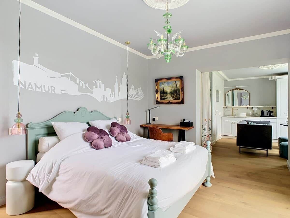 Een slaapkamer met een bed, een bureau, een stoel, een spiegel en stadsgezicht kunst aan de muur.