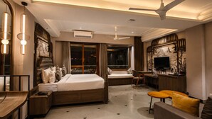 A hotel room with a bed, a desk, a sofa, a TV, and a ceiling fan. - The Luxury Tiger at Lake Pichola (Udaipur)