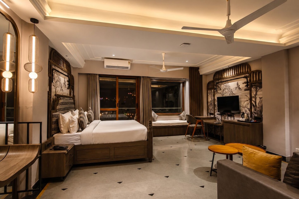 A hotel room with a bed, a desk, a sofa, a TV, and a ceiling fan.