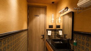 A narrow bathroom with a wooden ceiling, a ceiling fan, a sink with a black countertop, and patterned walls. - The Luxury Tiger at Lake Pichola (Udaipur)