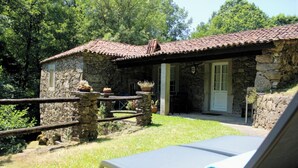 A stone building with a tiled roof, a small porch, and a lounge chair with a towel. - Casa Moinho da Levada: A Retreat on the Banks of the Coura River (Parada (Paredes De Coura))