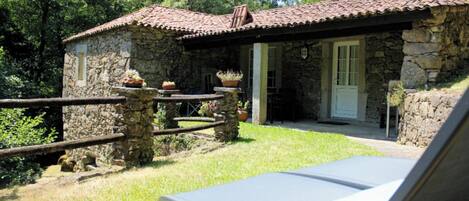 A stone building with a tiled roof, a small porch, and a lounge chair with a towel.