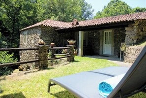 Un bâtiment en pierre avec un toit en tuiles, un petit porche et un fauteuil de jardin avec une serviette.