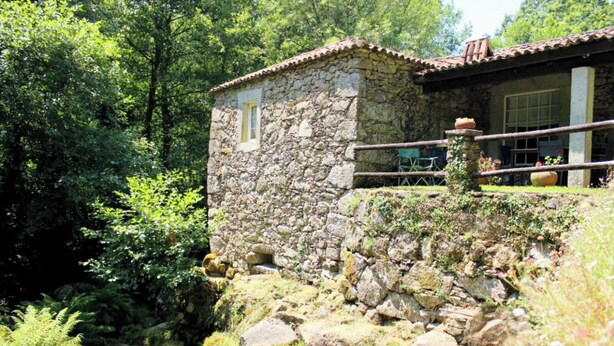 Un edificio de piedra con techo de tejas, una ventana pequeña y un balcón con sillas.