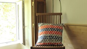 Una silla de madera con un cojín estampado, una puerta de madera y una ventana con vistas a la vegetación.
