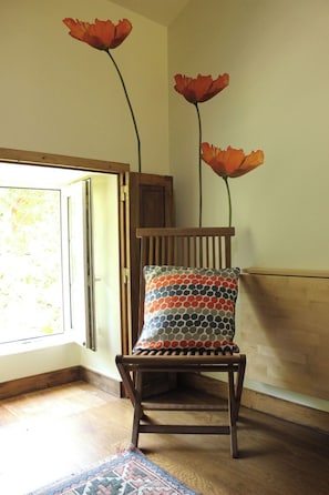 Une chaise en bois avec un coussin à motifs, une porte en bois et une fenêtre donnant sur la verdure.