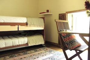 Une chambre avec un lit superposé, un petit bureau et une chaise, un tapis à motifs et une fenêtre donnant sur un paysage agréable.