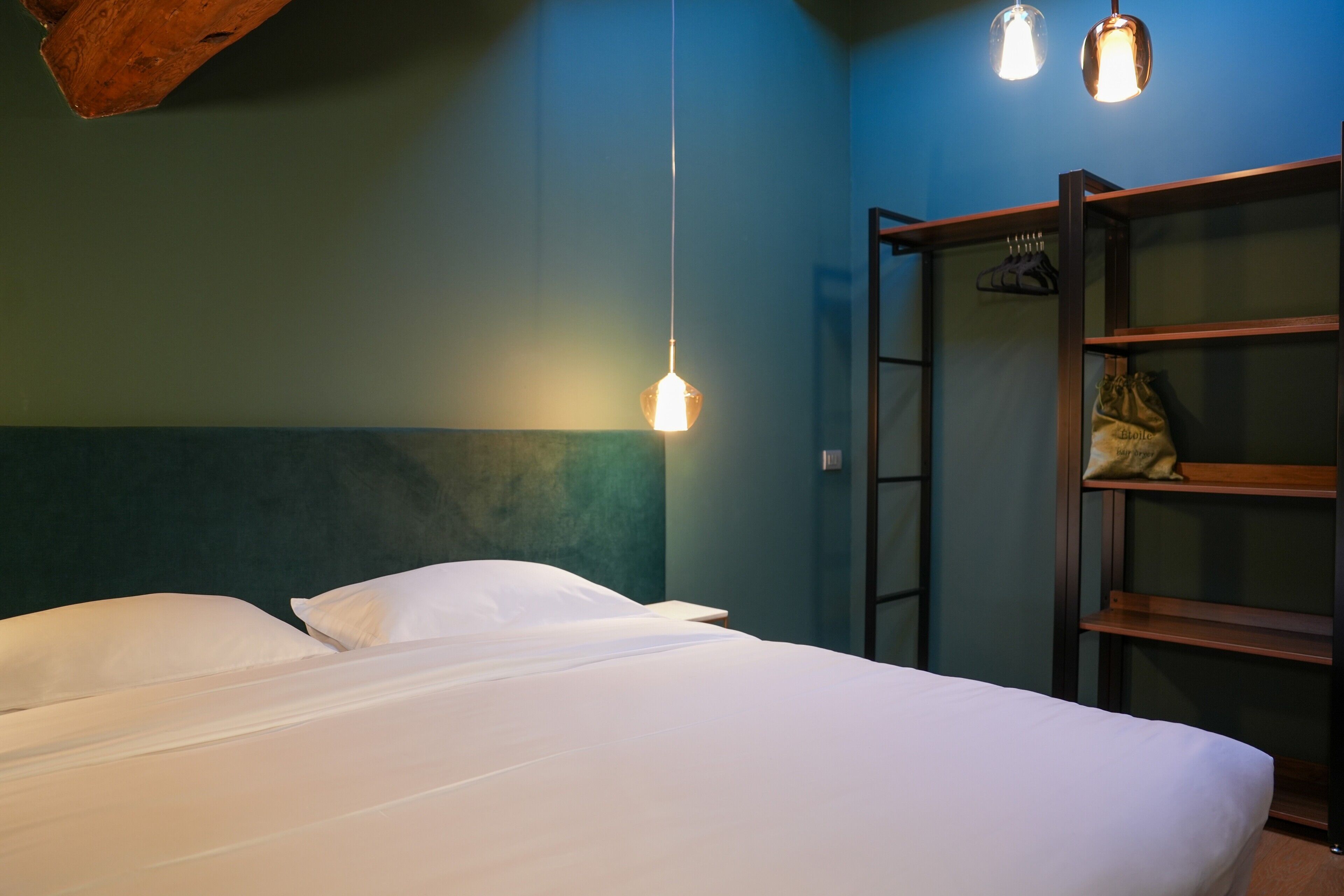 Un lit avec du linge de lit blanc, une tête de lit en bois et un luminaire suspendu.