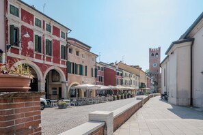 Un carrer amb seients a l'exterior, un edifici amb una torre de l'ajuntament, i un rètol que diu 'CALZATURE'.