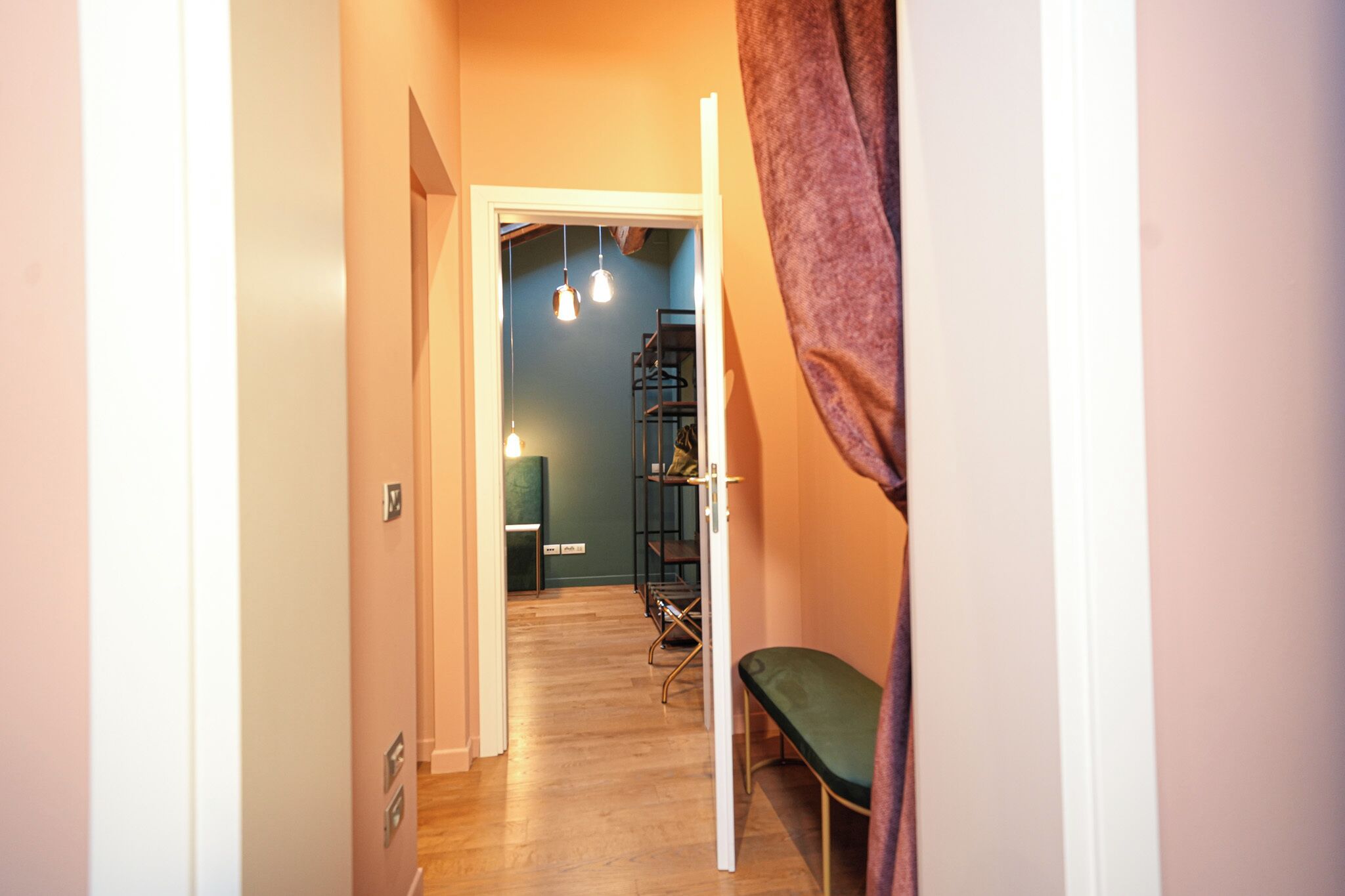 A hallway with a bench, a metal rack, and a door leading to another room.