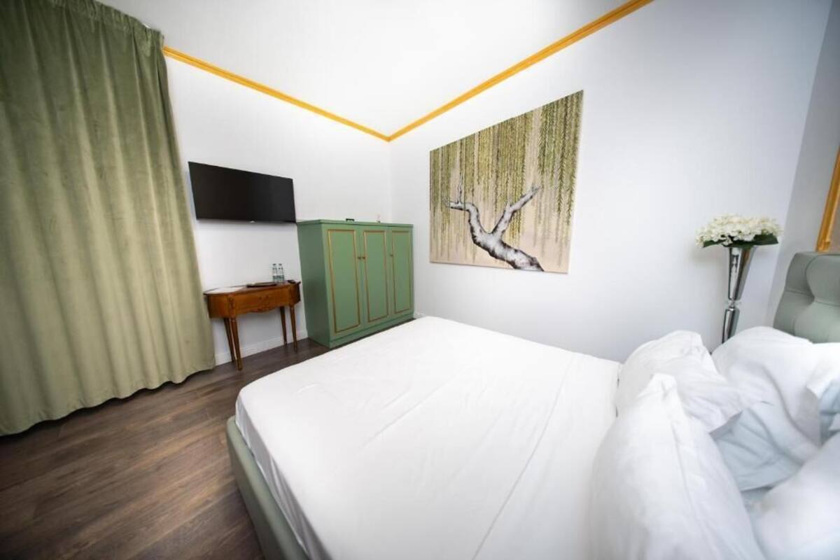 A hotel room with a bed, a television, a green cabinet, and a painting on the wall.