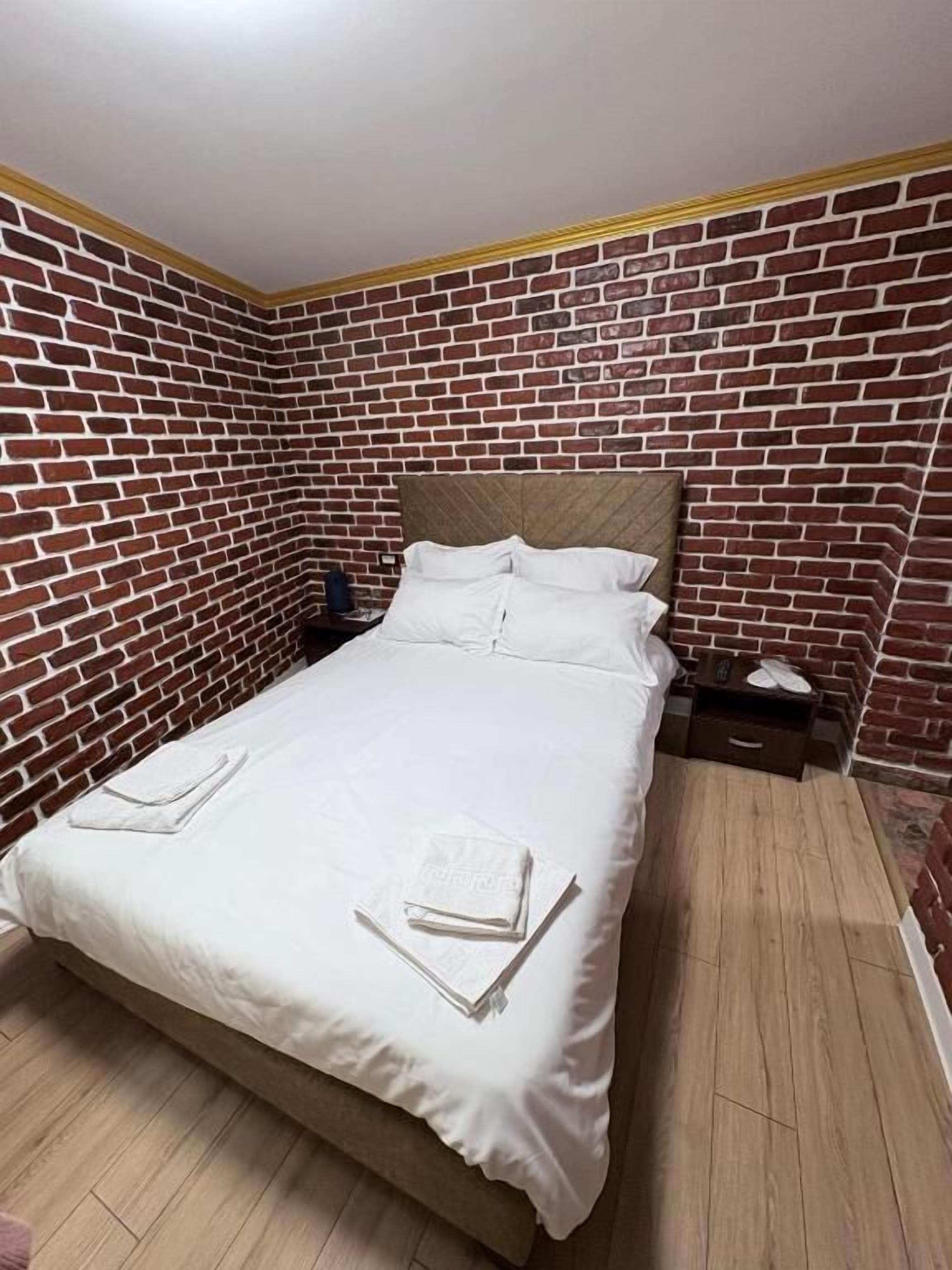 Una cama individual con ropa de cama blanca en una habitación con paredes de ladrillo y suelo de madera.