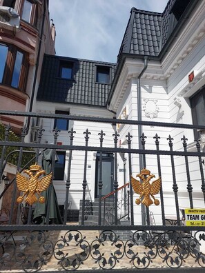 A building with a white facade, a black roof, and a black metal fence with golden eagle decorations.