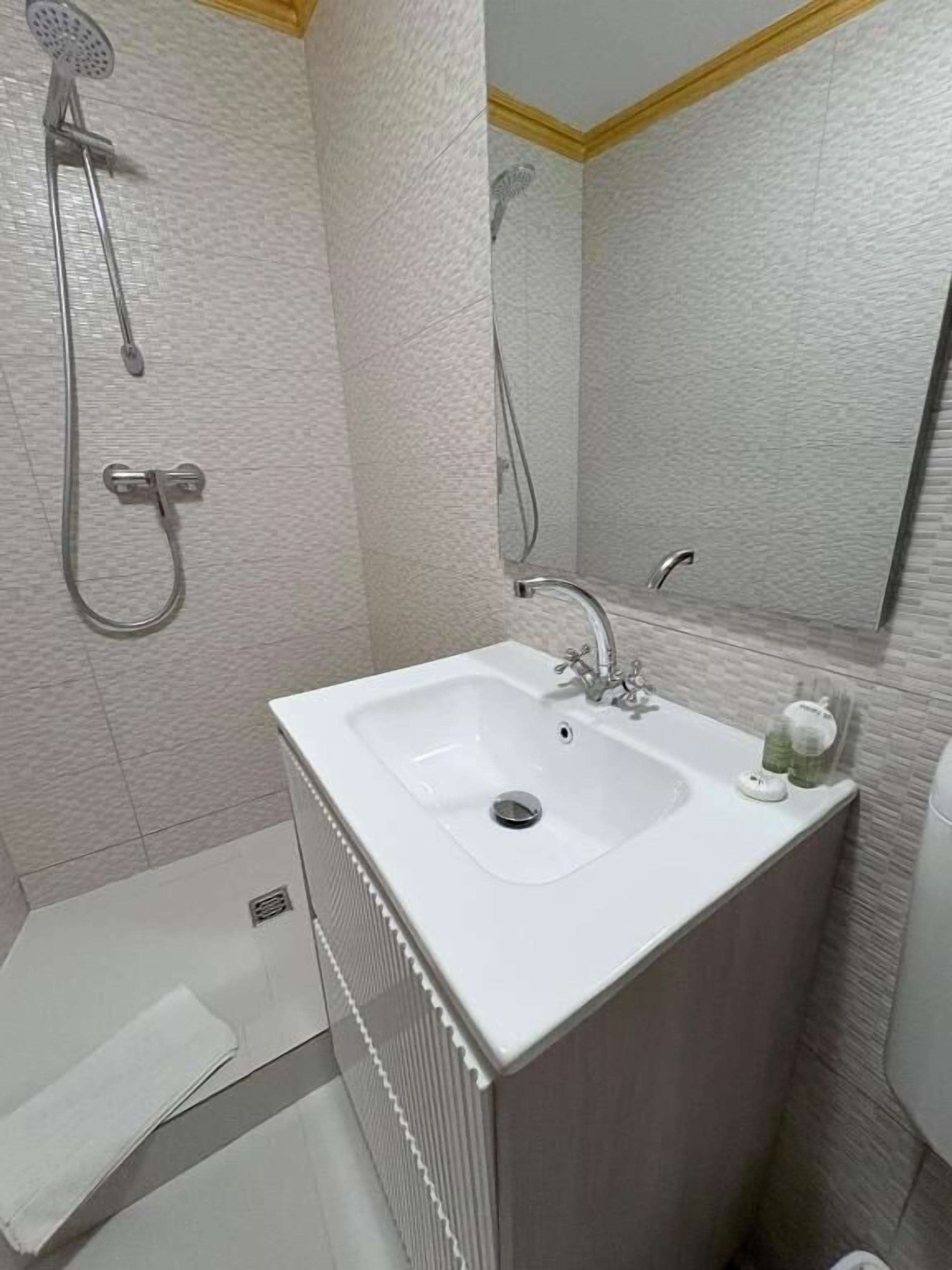 A bathroom with a white sink, a shower, and a mirror.
