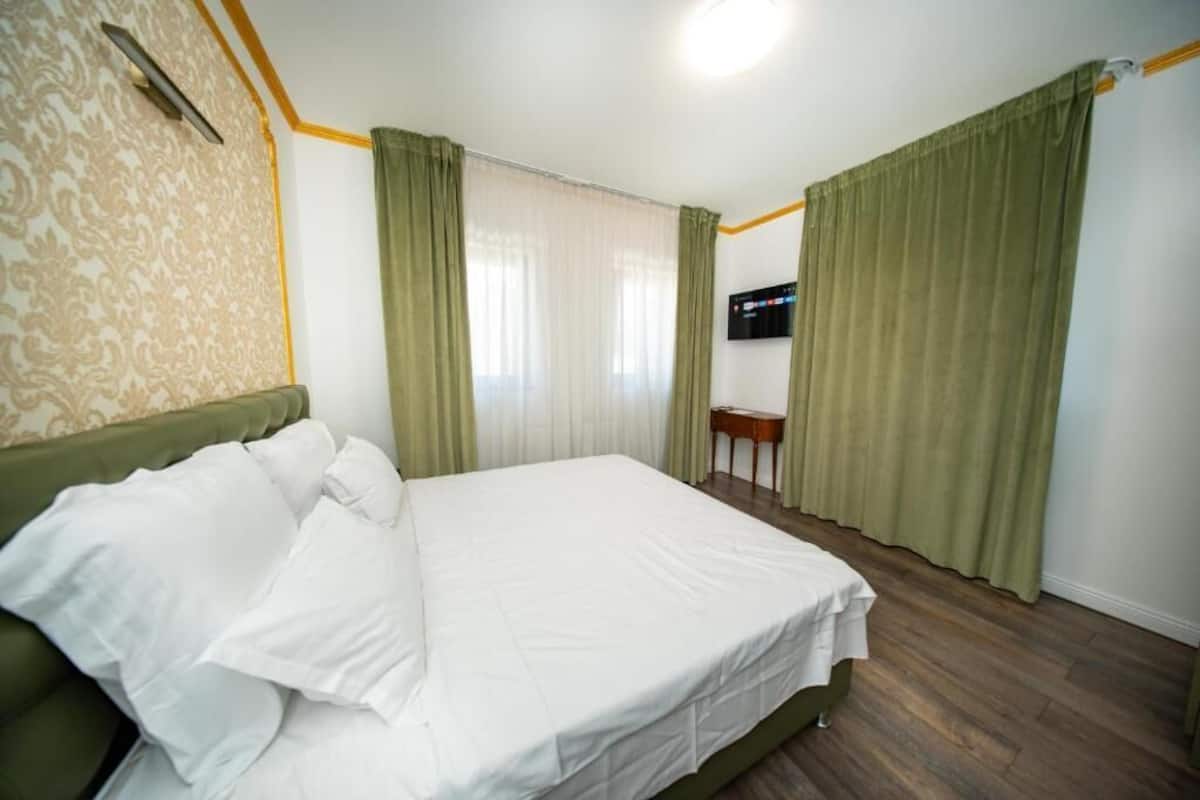 A bedroom with a bed, curtains, a television, and a small table.