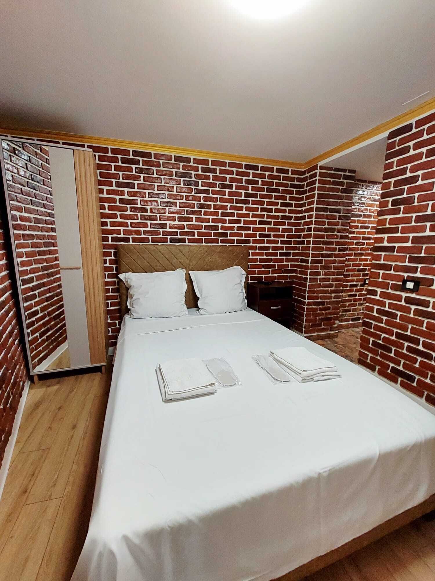 A single bed with white bedding, a wooden headboard, and a brick-patterned wall.