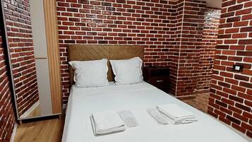 A single bed with white bedding, a wooden headboard, and a brick-patterned wall.