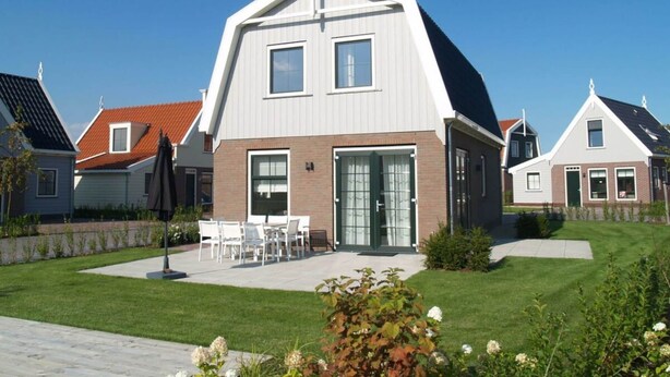 Een modern huis met een schuin dak, een veranda met stoelen en een verzorgd gazon.