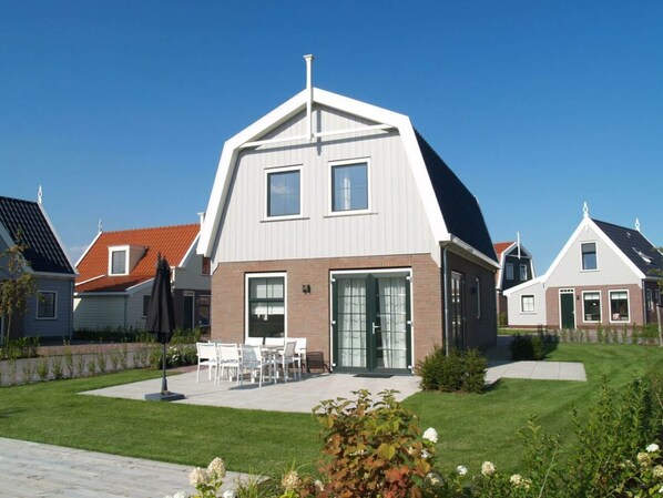 A modern house with a sloped roof, a front porch with chairs, and a well-maintained lawn. - Holiday Home in Uitdam With Terrace (Uitdam)