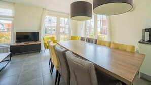 Een eetruimte met een lange tafel, stoelen en hanglampen.