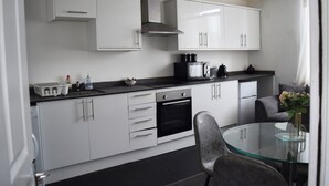 Een moderne keuken met witte kasten, een zwarte oven en een glazen eettafel.