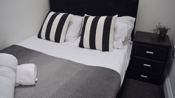 Een opgemaakt bed met gestreepte kussens, een grijze deken en een witte handdoek.