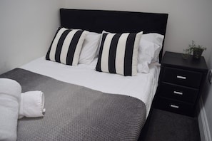 A neatly made bed with striped pillows, a grey blanket, and a white towel.
