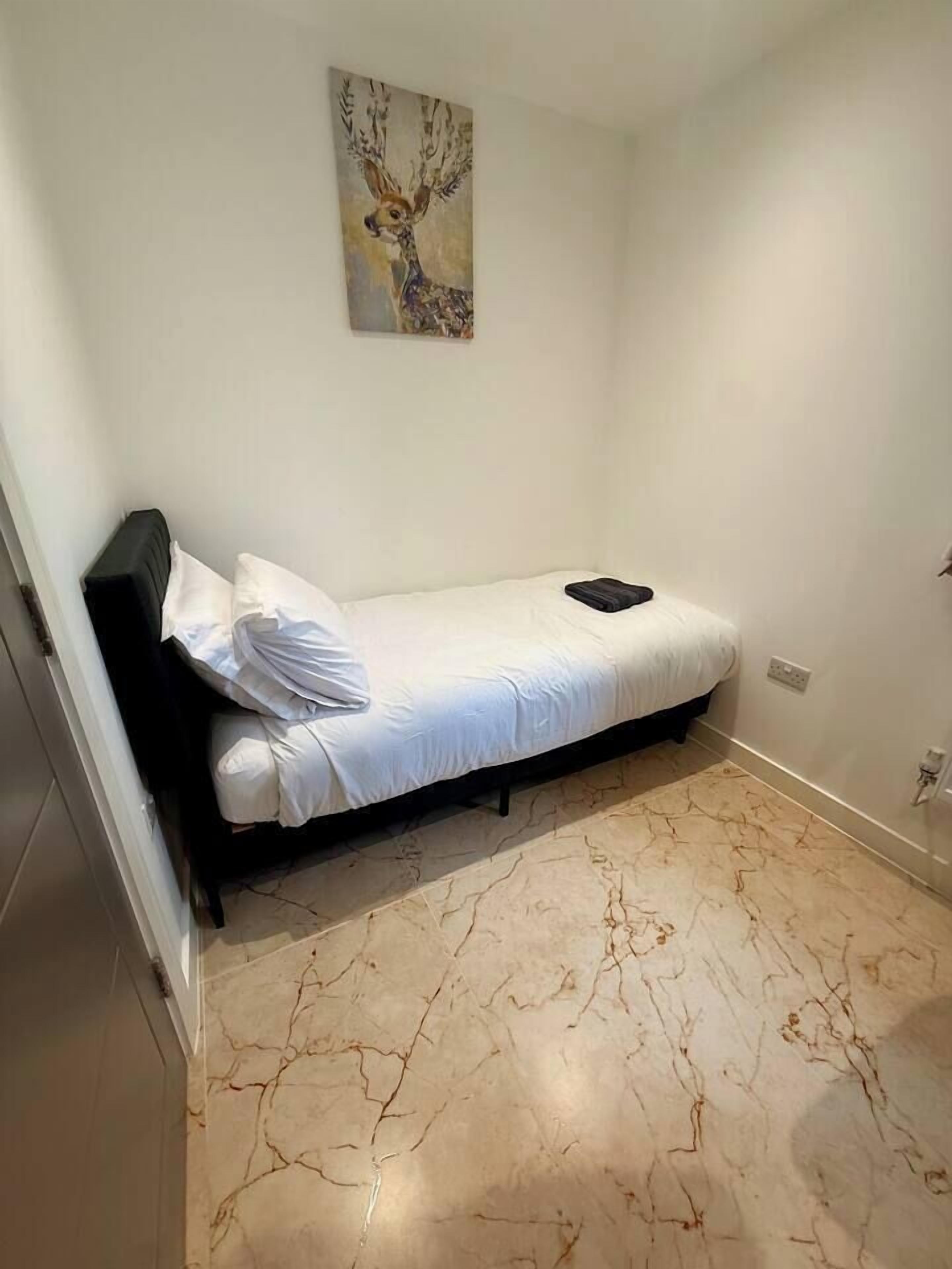 Habitació petita amb un llit individual, sòl de marbre, un quadre a la paret i un panell de capçalera negre.