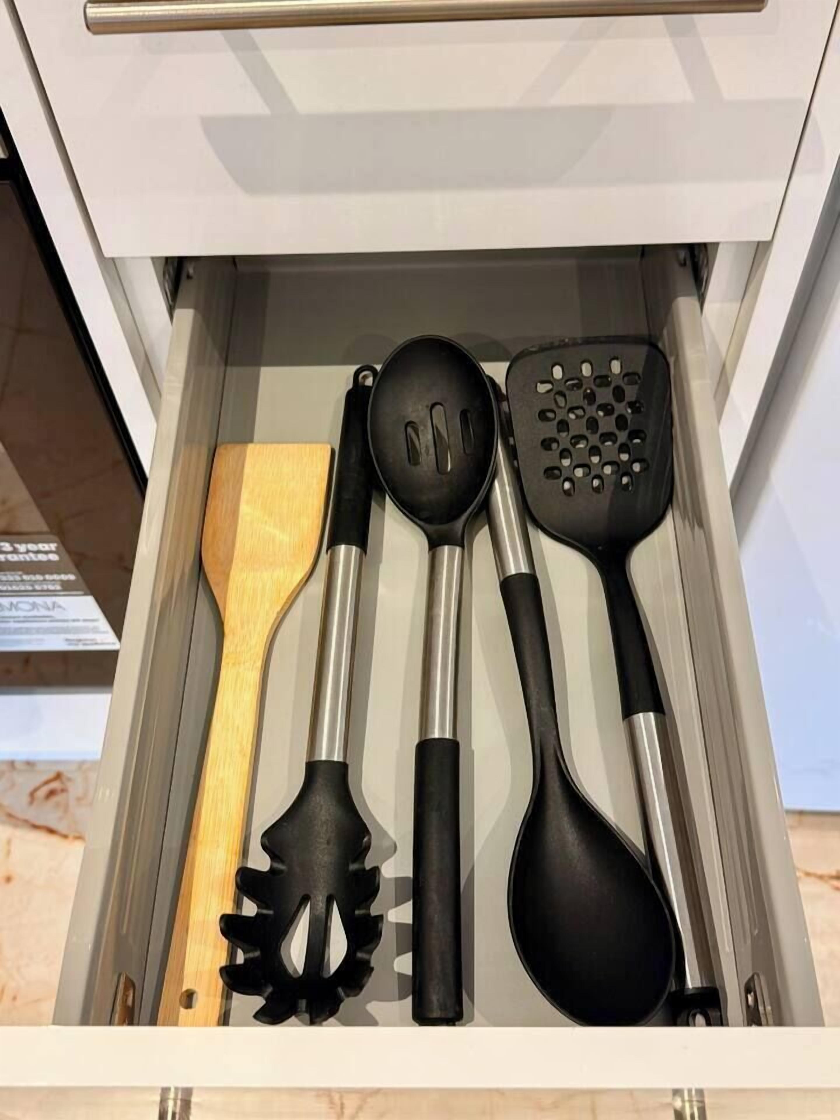 Een lade met keukengerei, waaronder een houten spatel, een zwarte spatel met gaten, een zwarte opscheplepel en een zwarte soeplepel.