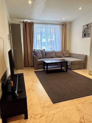 Een woonkamer met een bank, een salontafel, een televisie en een raam met gordijnen.